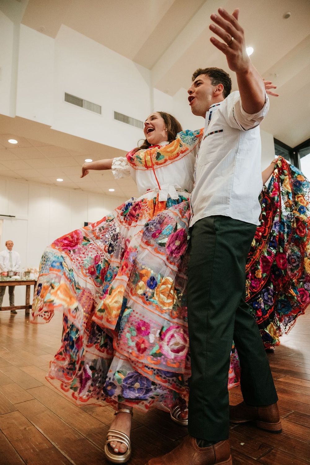 Dancing guests in colorful floral dresses twirling on wooden dance floor.