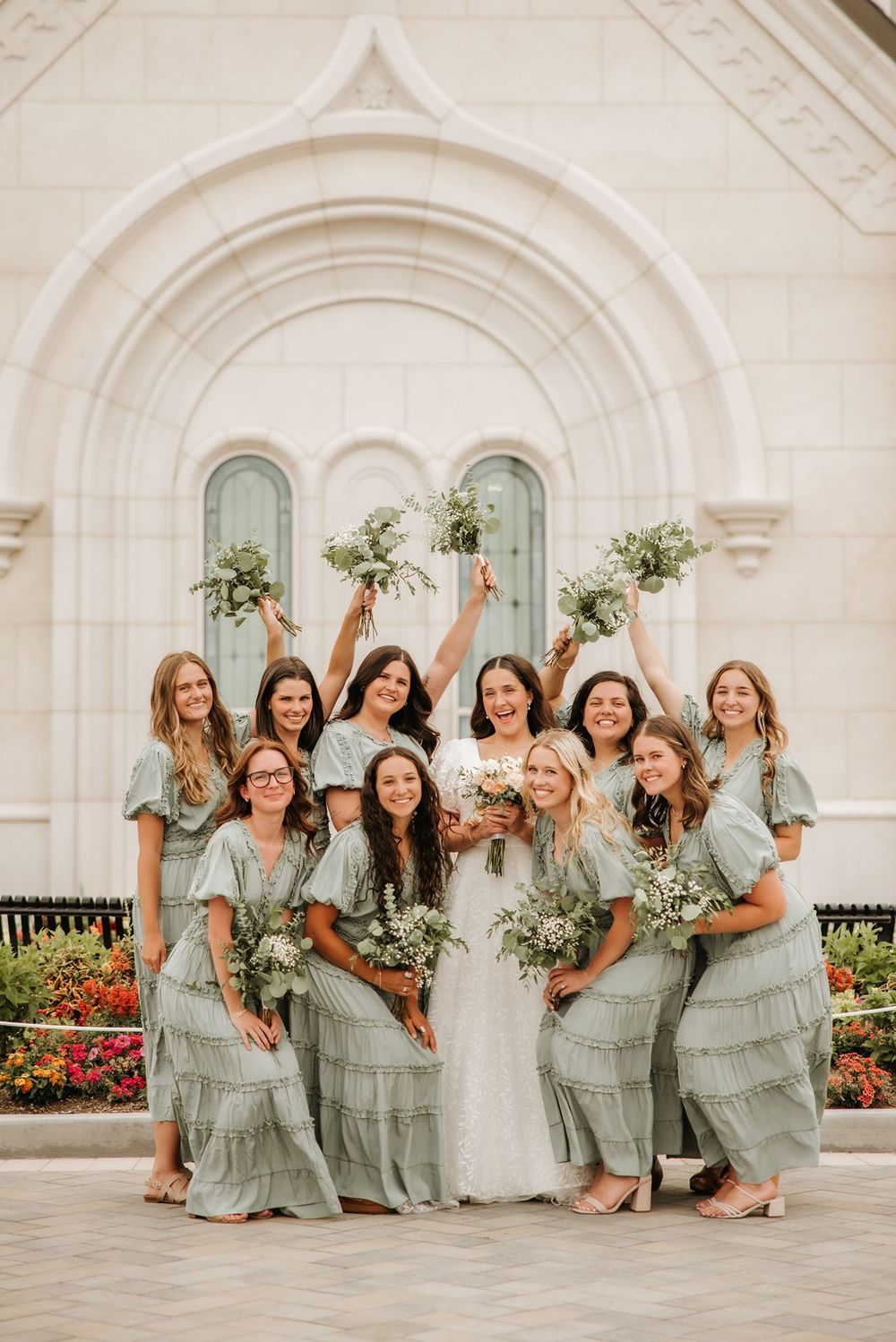 Bridesmaids in sage green tiered dresses pose with bride in front of taylorsville utah temple.