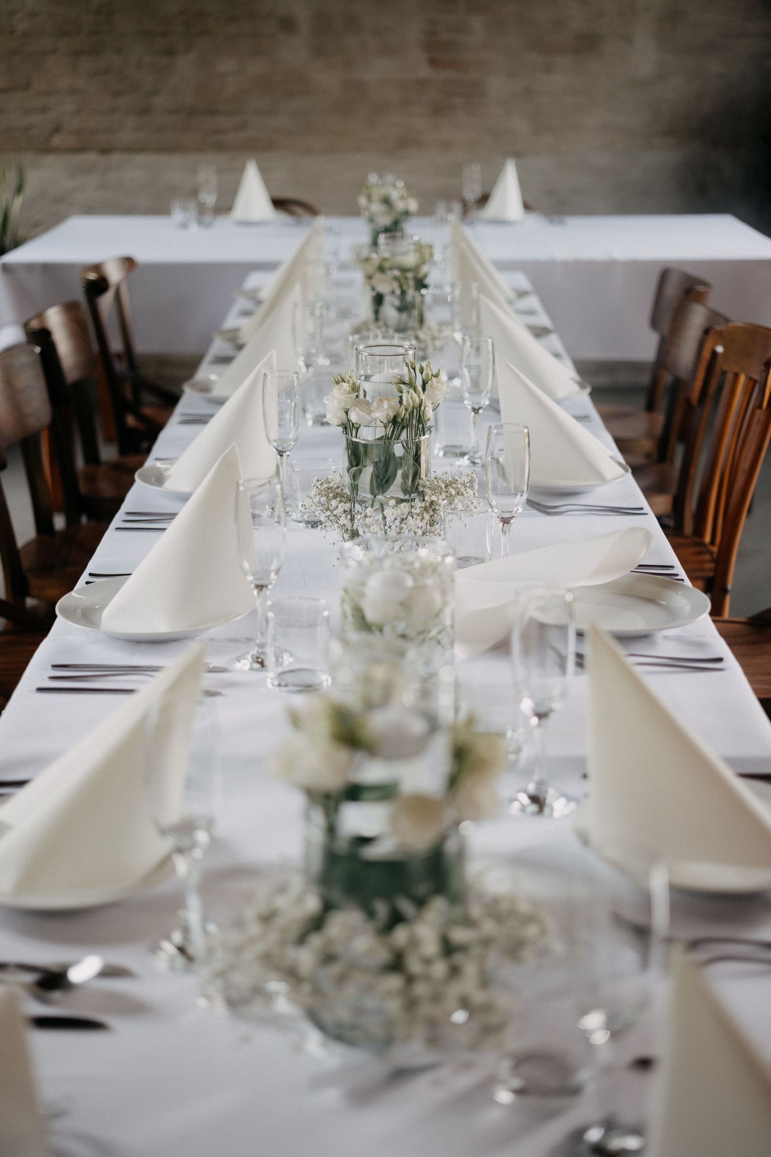 Long dining table with white tablecloth decorated with delicate floral centerpieces and place settings.