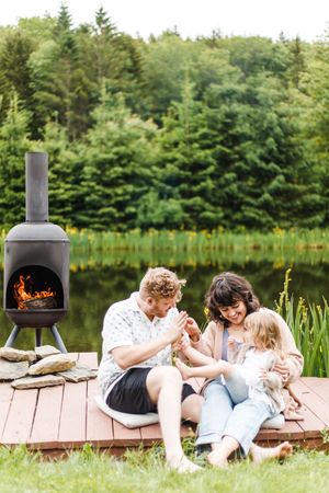 A cozy outdoor scene on a dock with a chiminea fireplace and lake view surrounded by evergreen trees.
