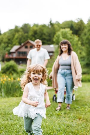A joyful child runs through a grassy field with yellow flowers and a rustic house in the background.