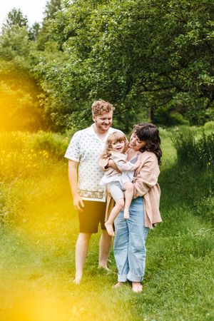 A family shares a tender moment together while standing on a grassy path with trees and golden sunlight in the background.