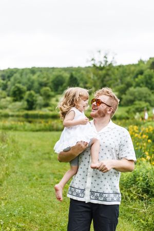 Family playing together in a sunny field with wildflowers and green grass.
