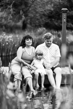 Family sitting together with their feet dangling in a lake on a summer day, creating a relaxing outdoor moment.