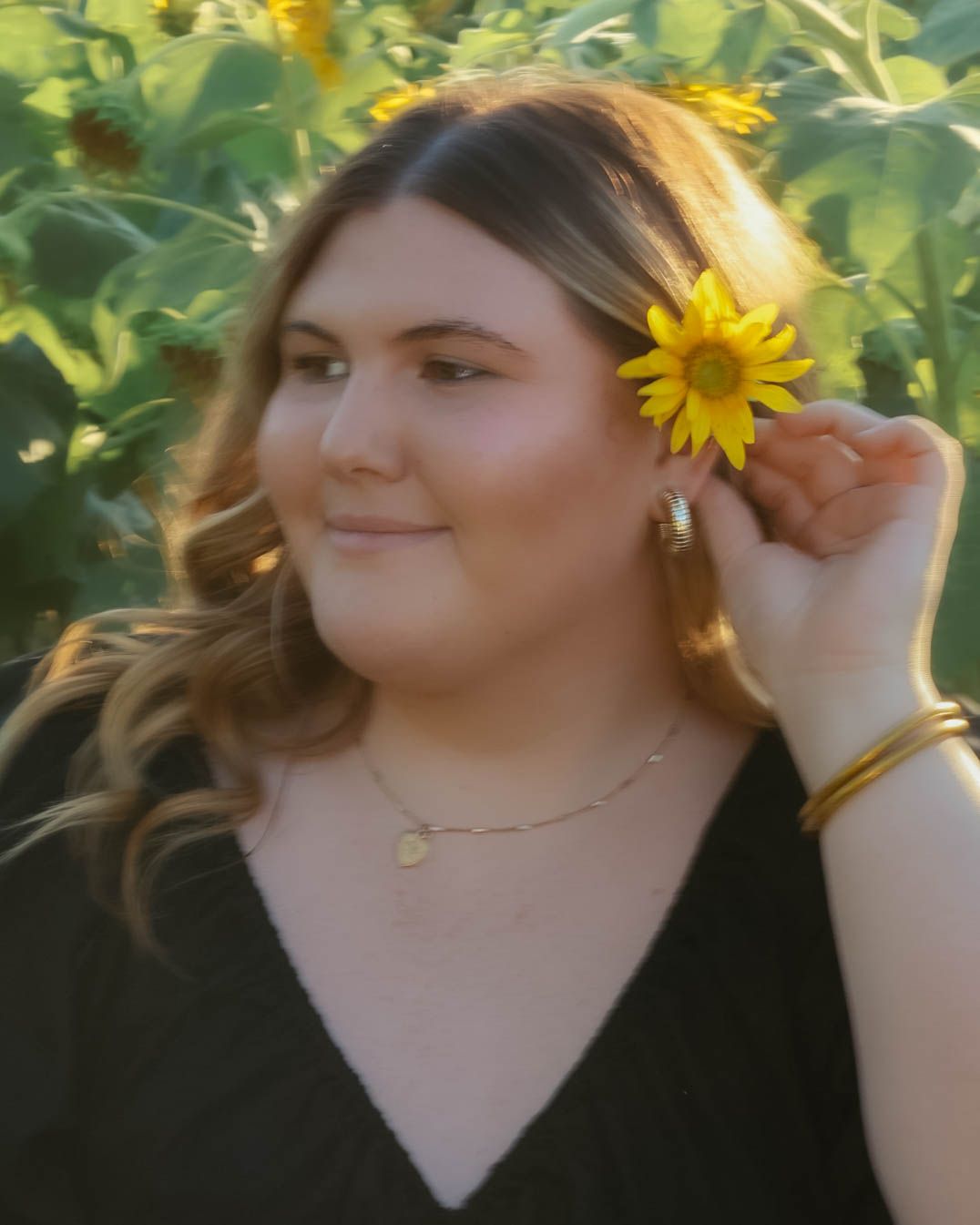 A person posing with sunflowers in a garden setting during golden hour.