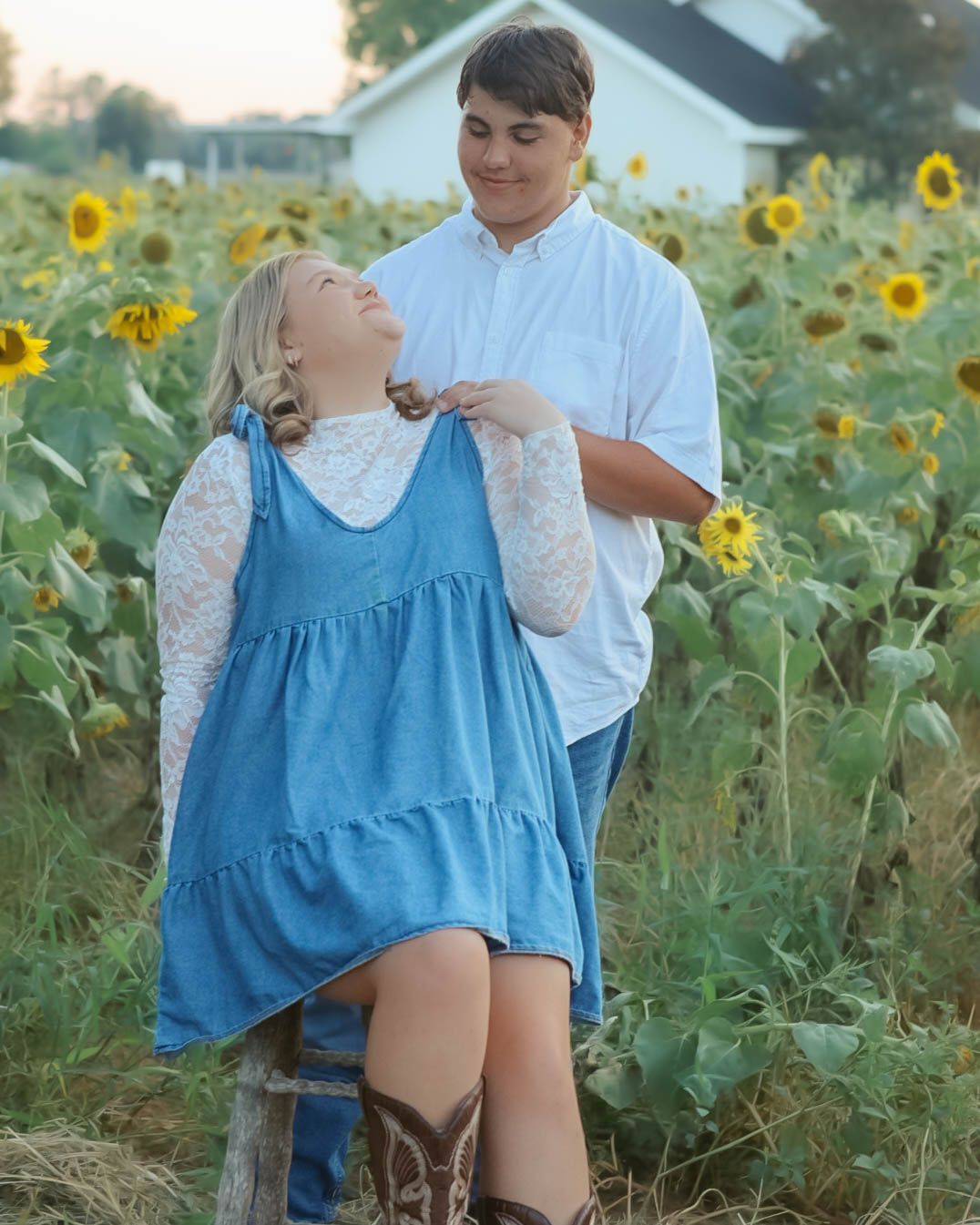 A couple posing in a sunflower field wearing coordinated blue and white outfits.