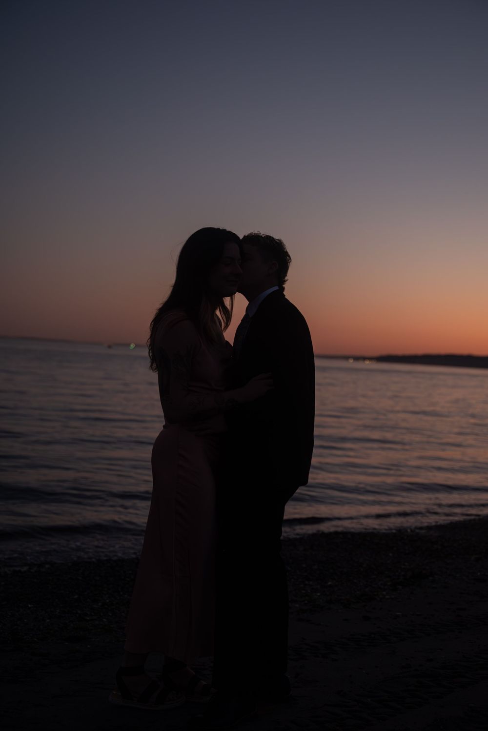 Silhouetted couple sharing an intimate moment against a dramatic sunset beach backdrop.