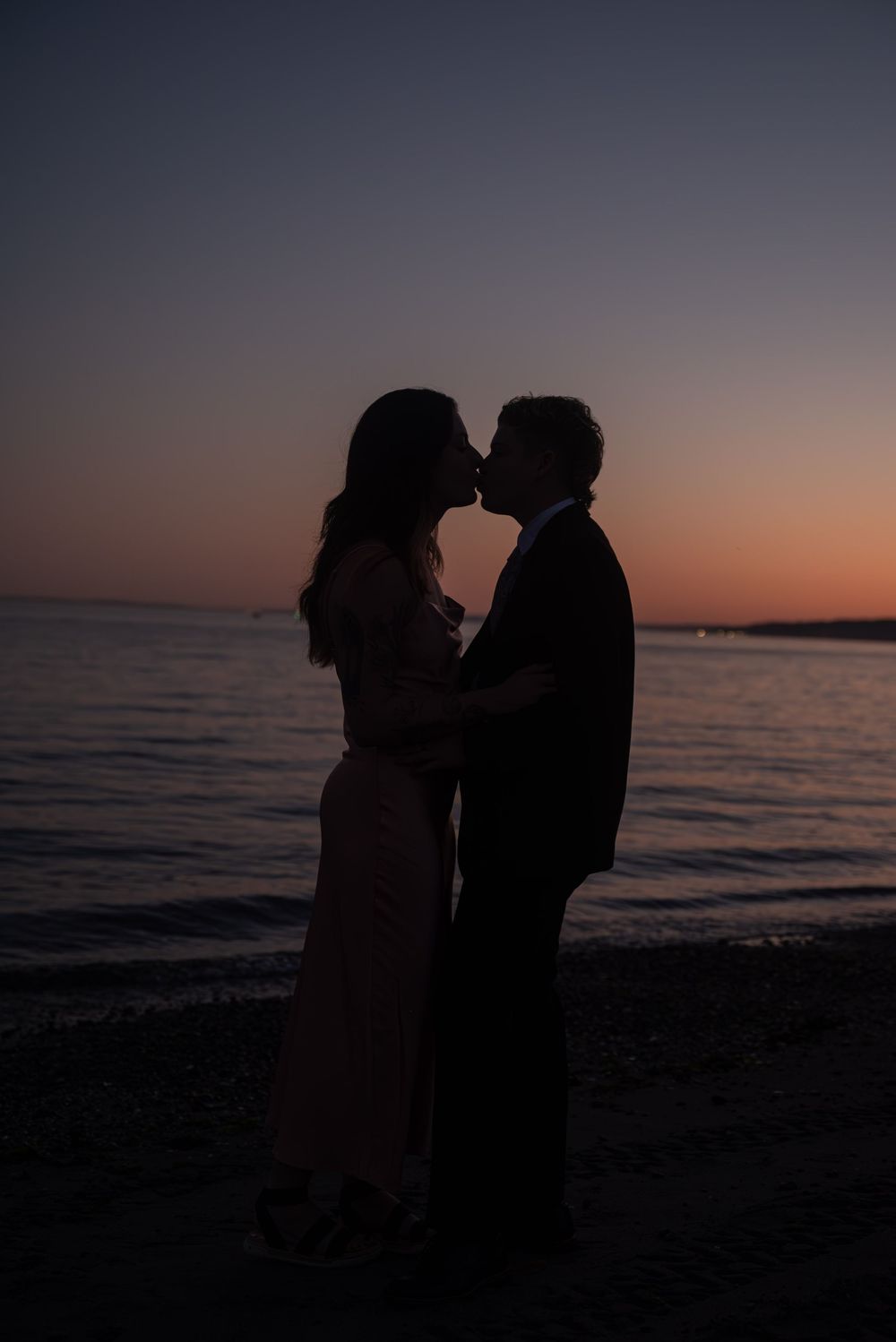 Silhouetted couple shares romantic moments at sunset on a beach with ocean waves in the background.