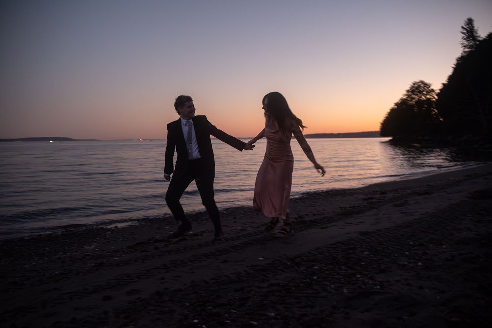 Silhouettes of a couple walking along a scenic beach shoreline at sunset with golden light reflecting on the water.