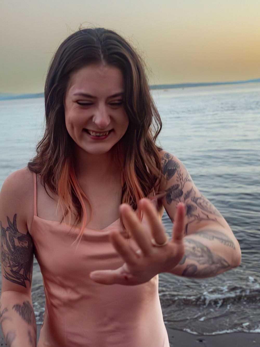 Person in pink top showing excited reaction at beach during sunset.