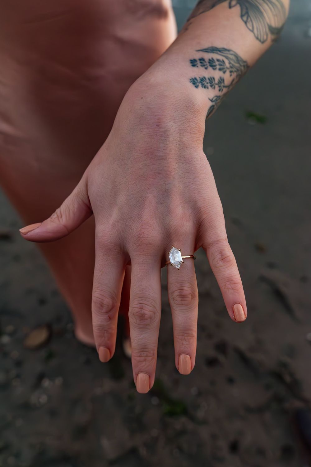 Close-up of a hand wearing an engagement ring with a delicate leaf tattoo visible on the wrist.