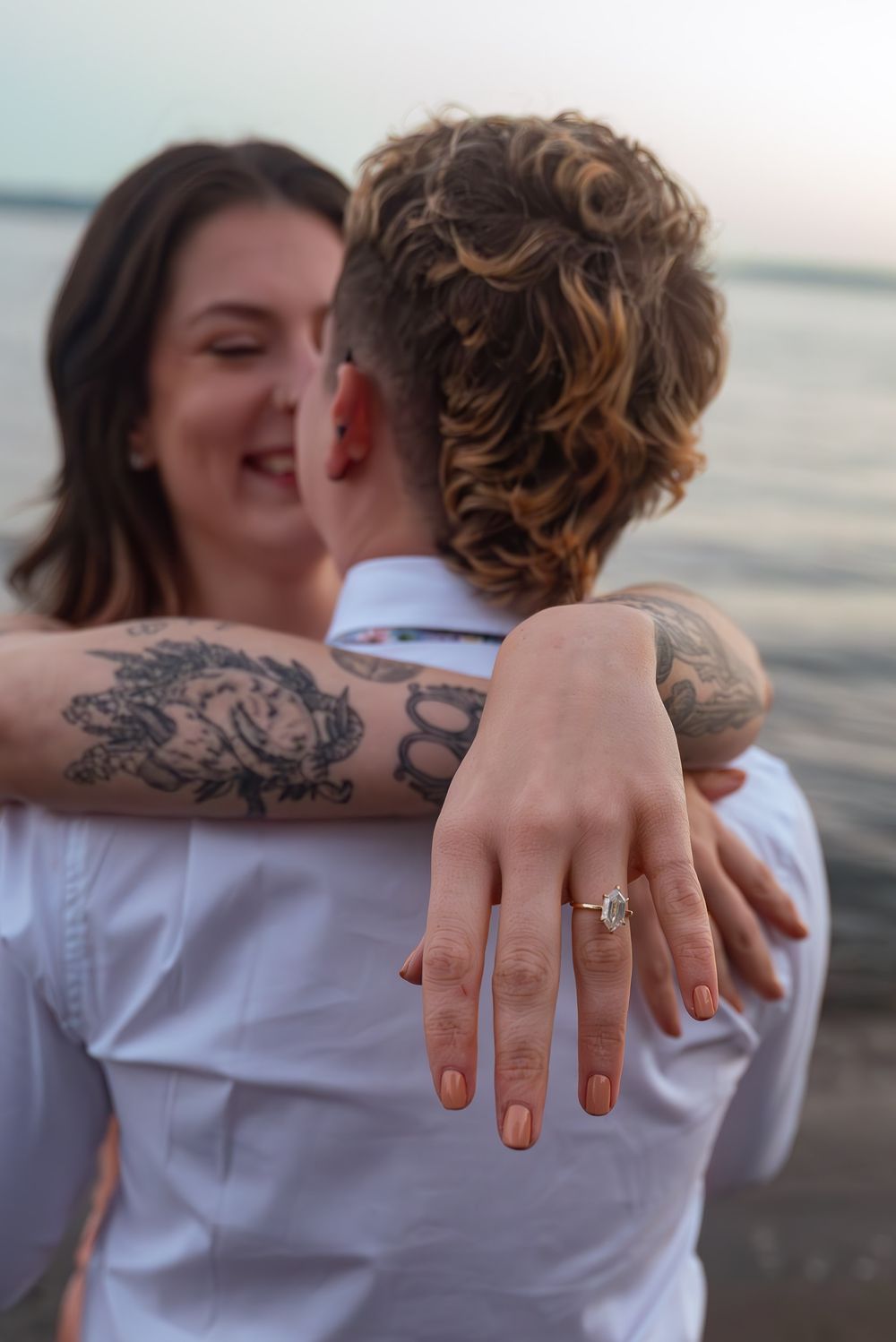 Close up view of hands with engagement ring embracing against sunset beach background.