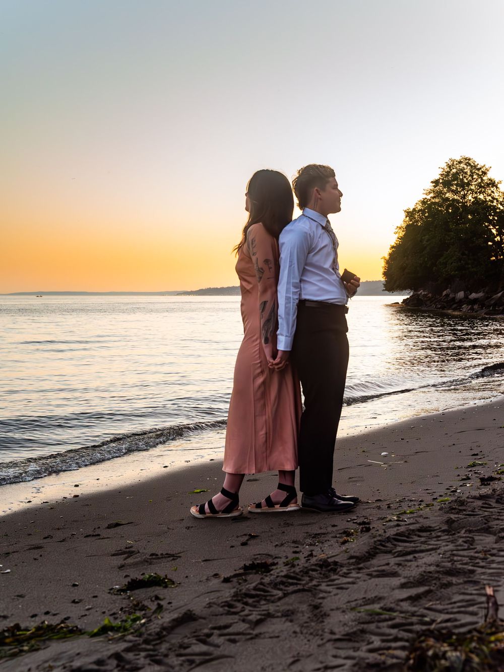Couple in formal attire sharing intimate moment on sandy beach during golden hour sunset.