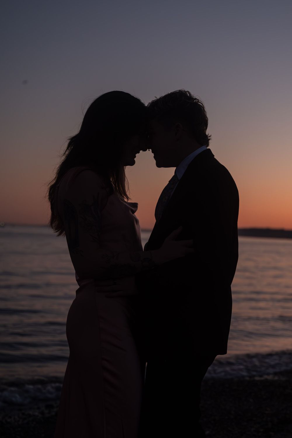 Silhouetted couple sharing an intimate moment against a sunset beach backdrop.