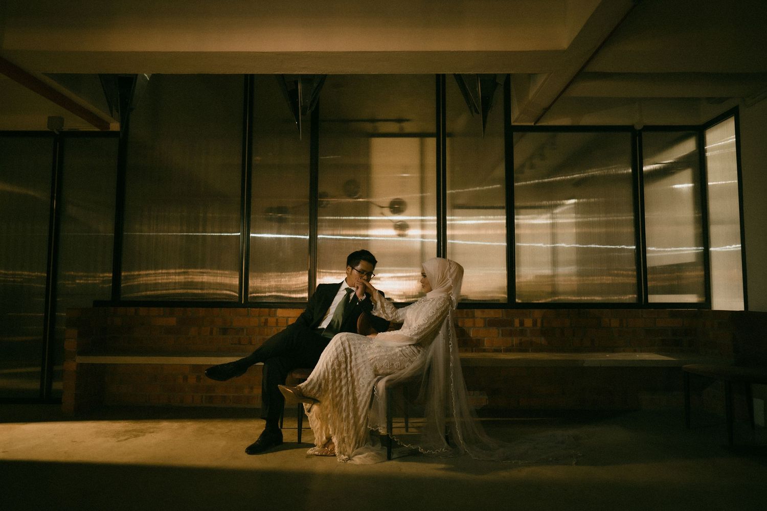 Couple sits intimately in dramatic moody industrial setting with warm amber lighting.