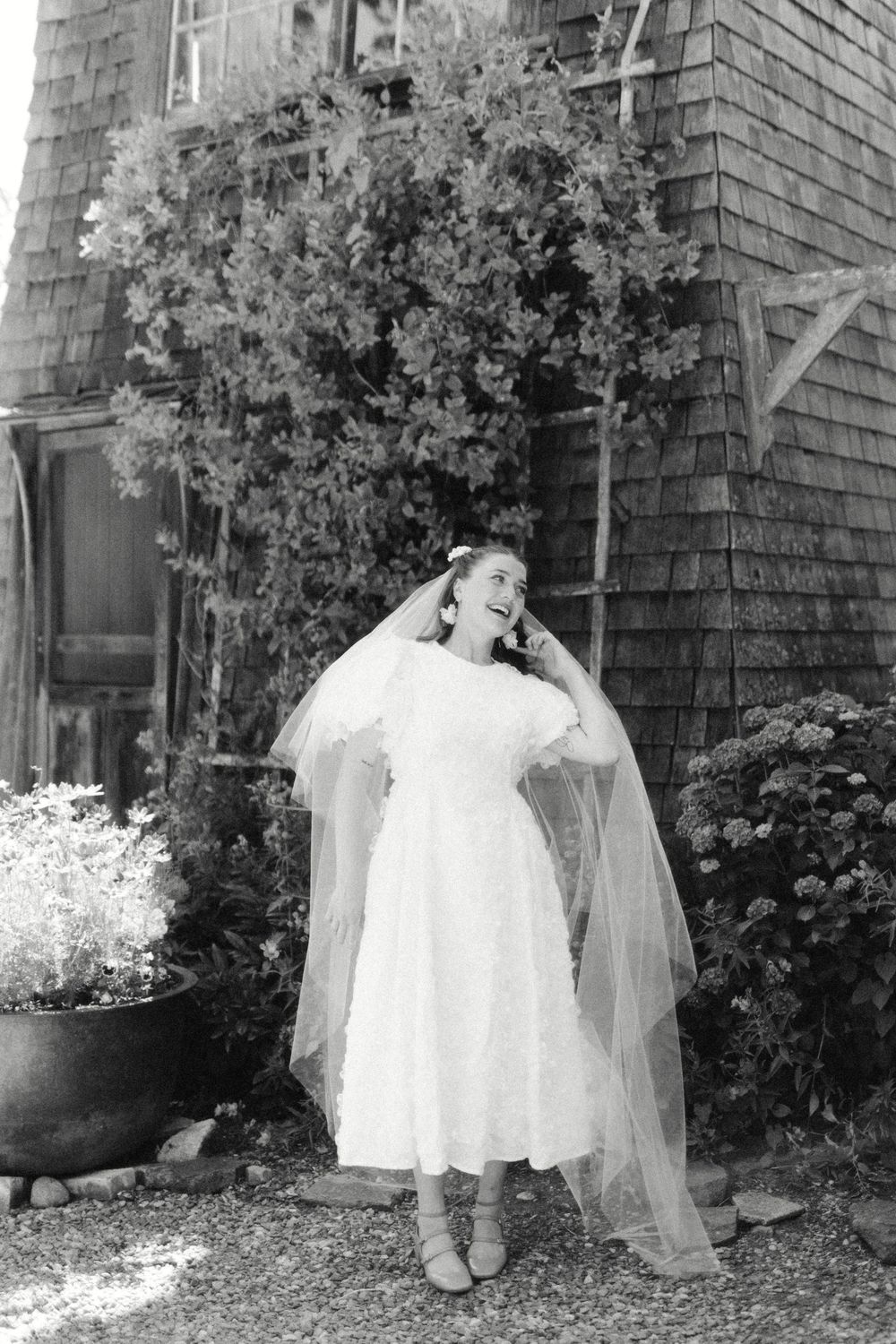 Outdoor wedding photos against a brick building with shingle siding and garden foliage.