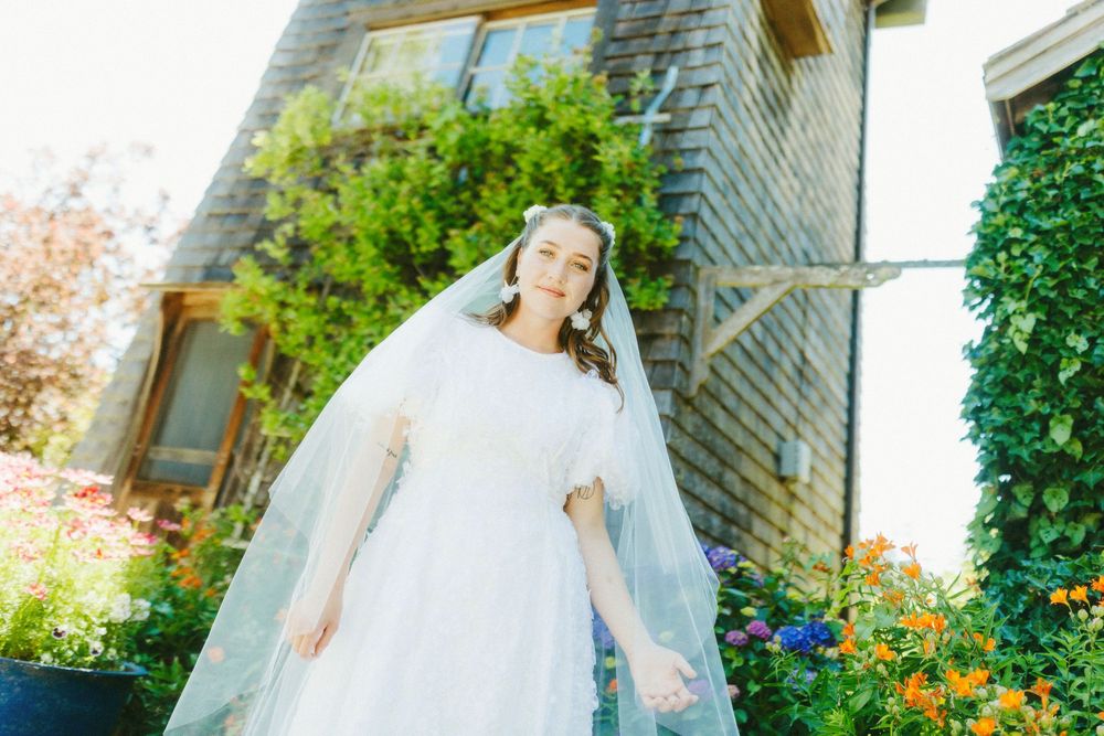Wedding party poses in front of a rustic stone building surrounded by lush greenery.