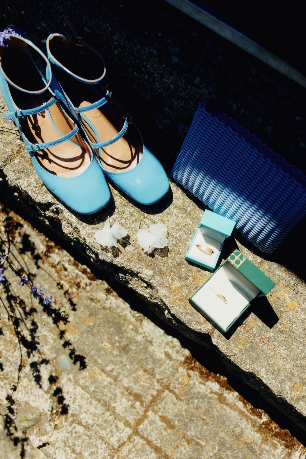 Light blue bridal shoes and wedding ring box on stone surface.