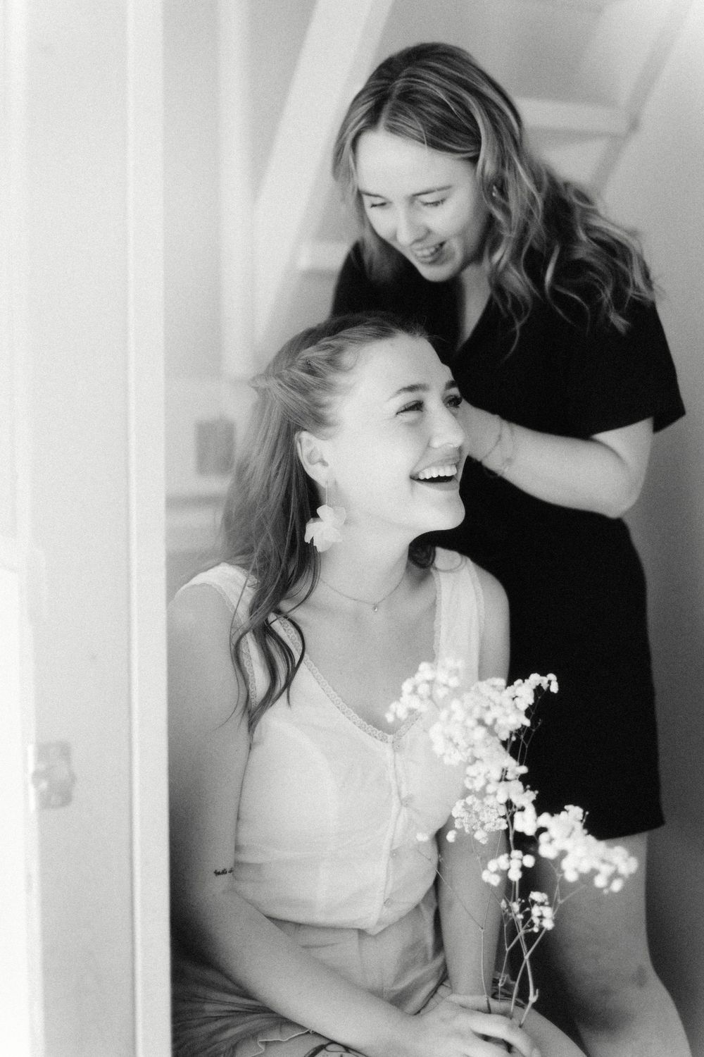 Black and white photos show joyful laughter during wedding preparations with delicate white flowers.
