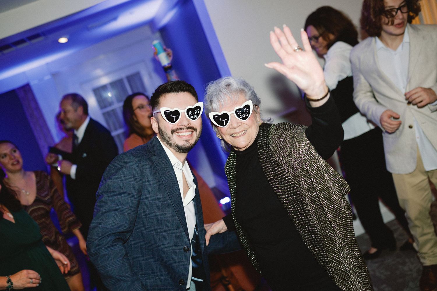 Party guests wearing sunglasses pose at reception with blue lighting.