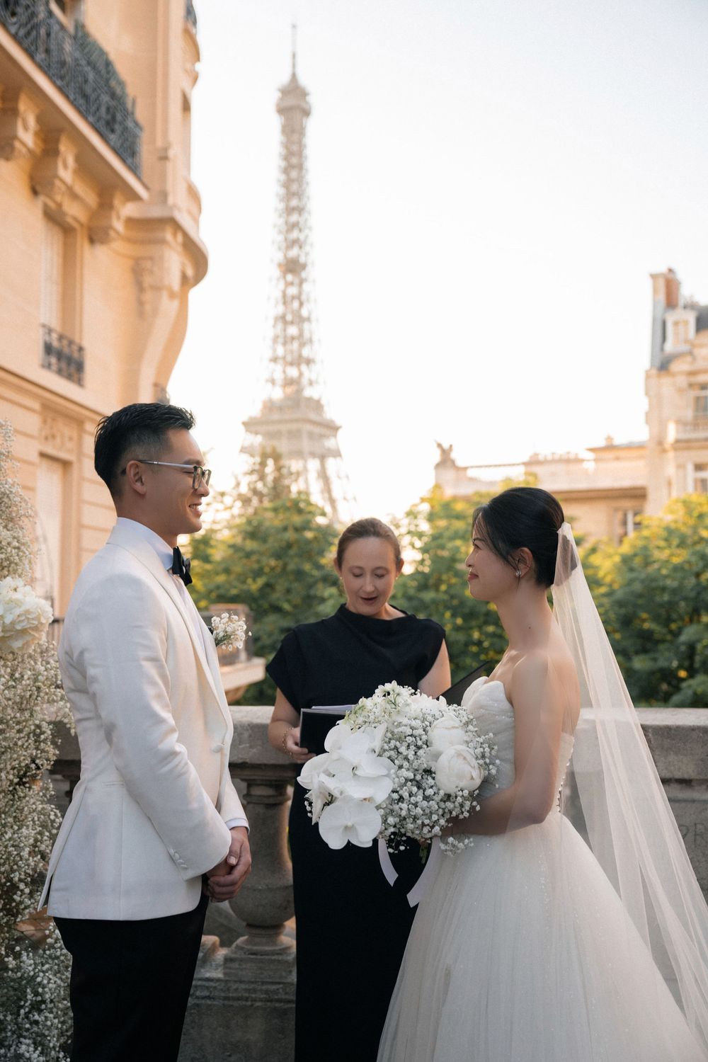 An intimate wedding ceremony taking place on a balcony in Paris with white floral decorations.