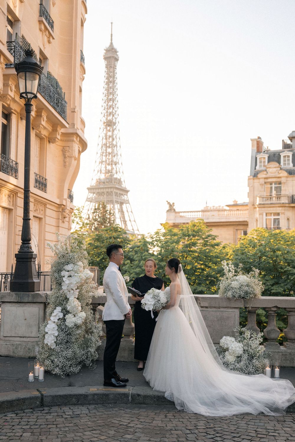 A romantic wedding photoshoot in Paris with the Eiffel Tower visible in the background and white floral arrangements.