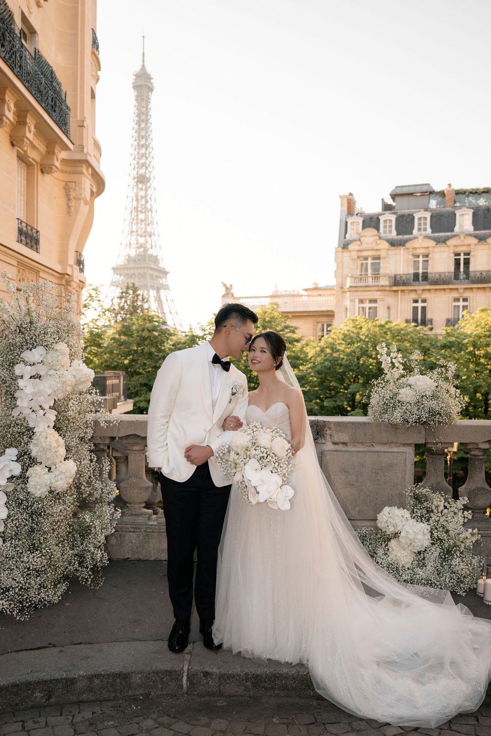 Romantic wedding portrait on Paris balcony with Eiffel Tower and classic architecture in background.