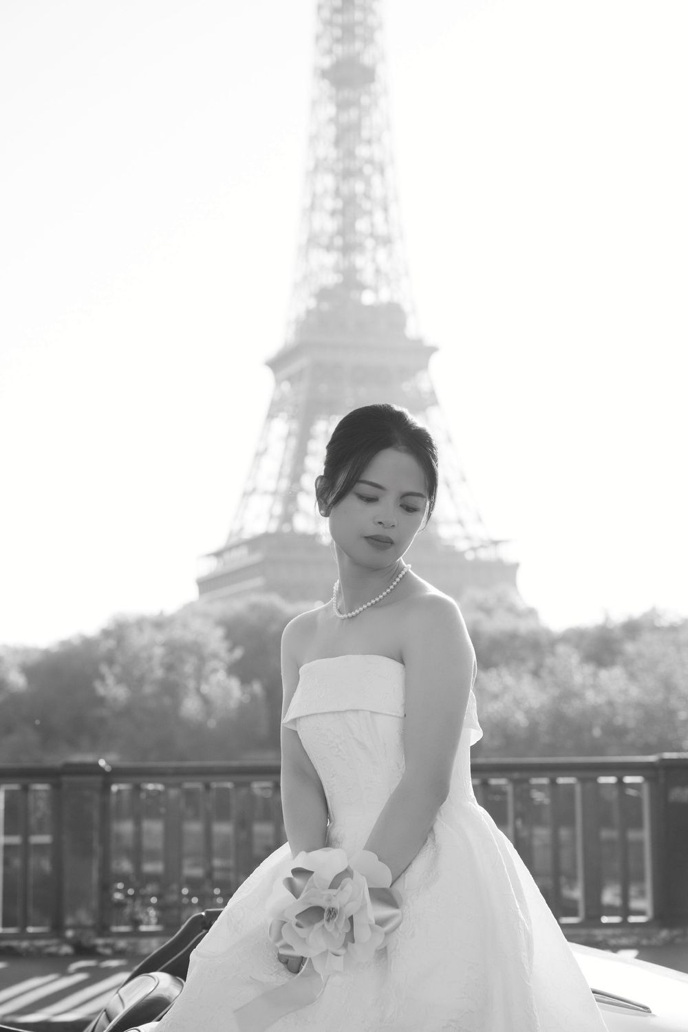 A bride in a strapless gown poses elegantly with the Eiffel Tower backdrop in black and white.