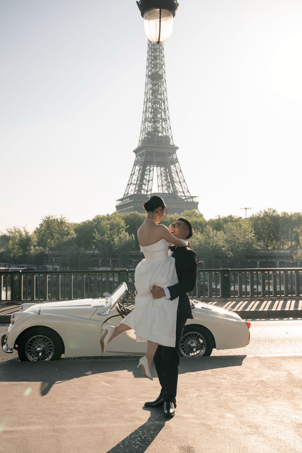 A romantic moment captured in front of the Eiffel Tower with a vintage white automobile.