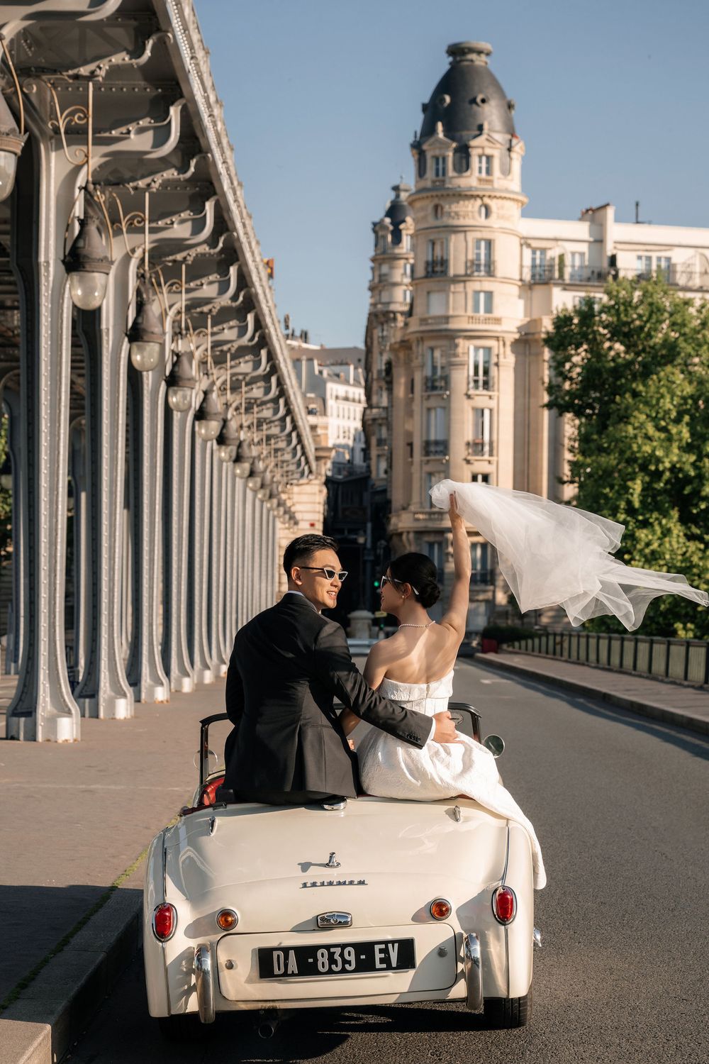 A vintage white convertible car parked along a colonnade with ornate architecture in the background.
