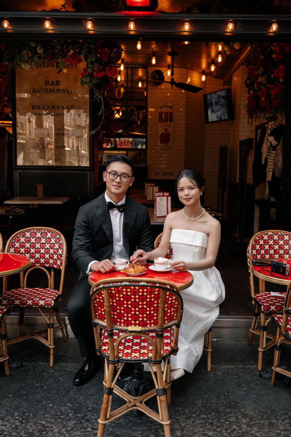 Newlyweds enjoy refreshments at a French bistro with traditional rattan chairs.