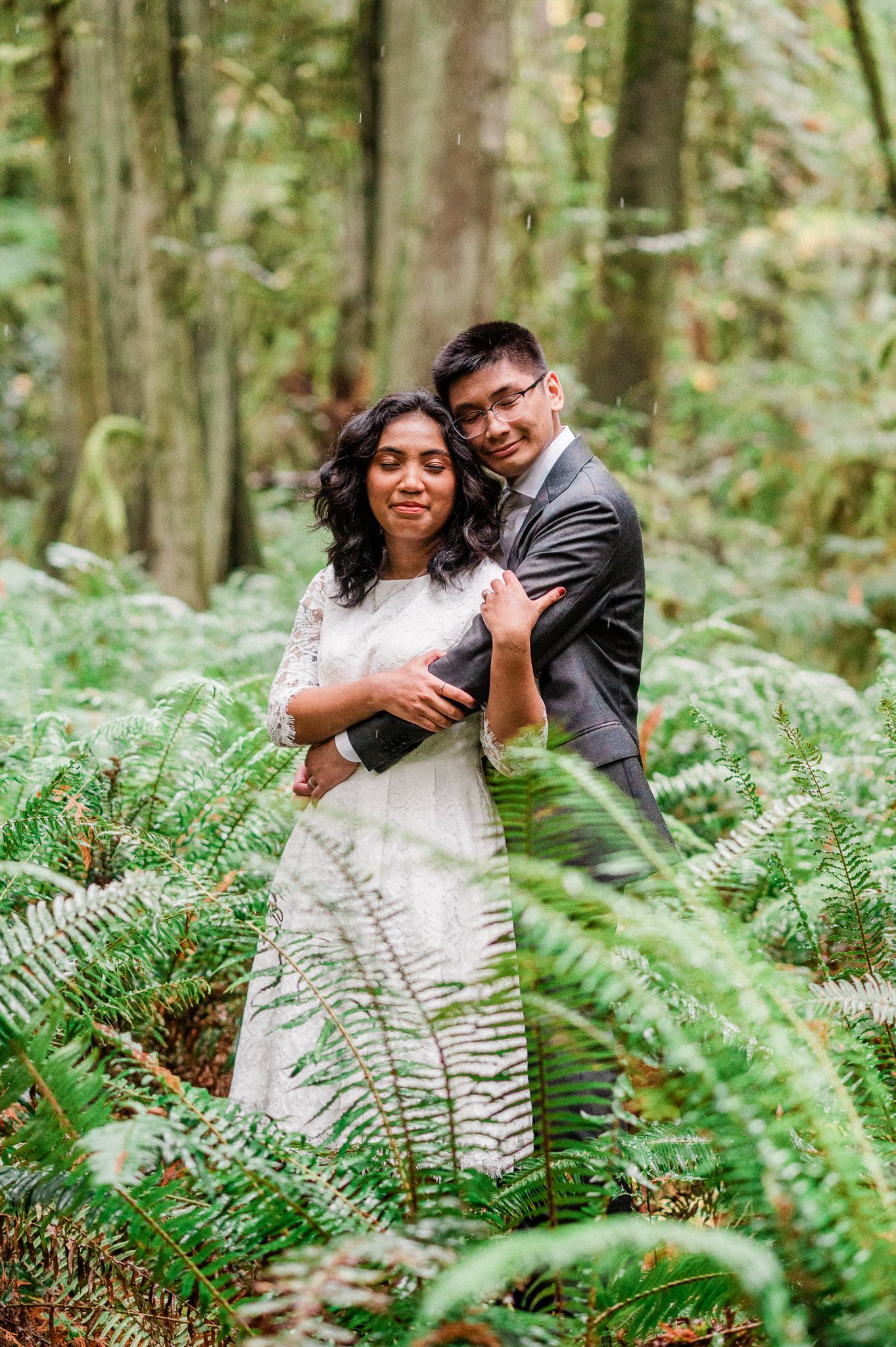 A couple shares a romantic embrace among lush green ferns in a peaceful forest during their Bainbridge Island Elopement.