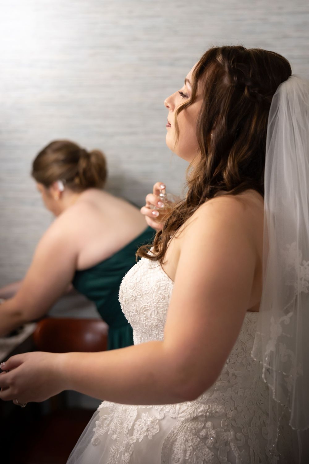 A bride in a white lace dress laughs joyfully while getting ready on her wedding day.