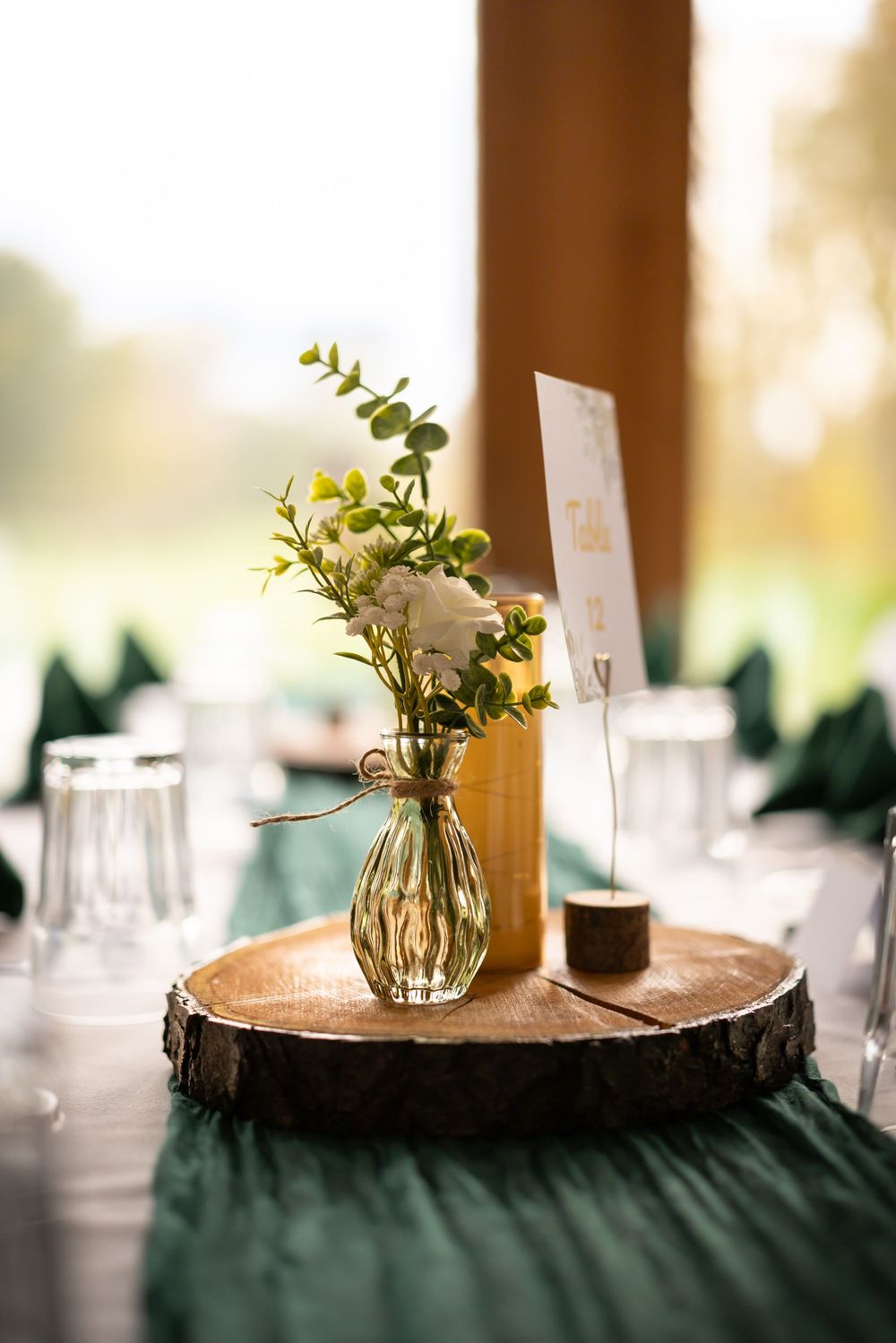 Rustic wood slice centerpieces with small glass vases holding delicate white flowers on dark tablecloths.