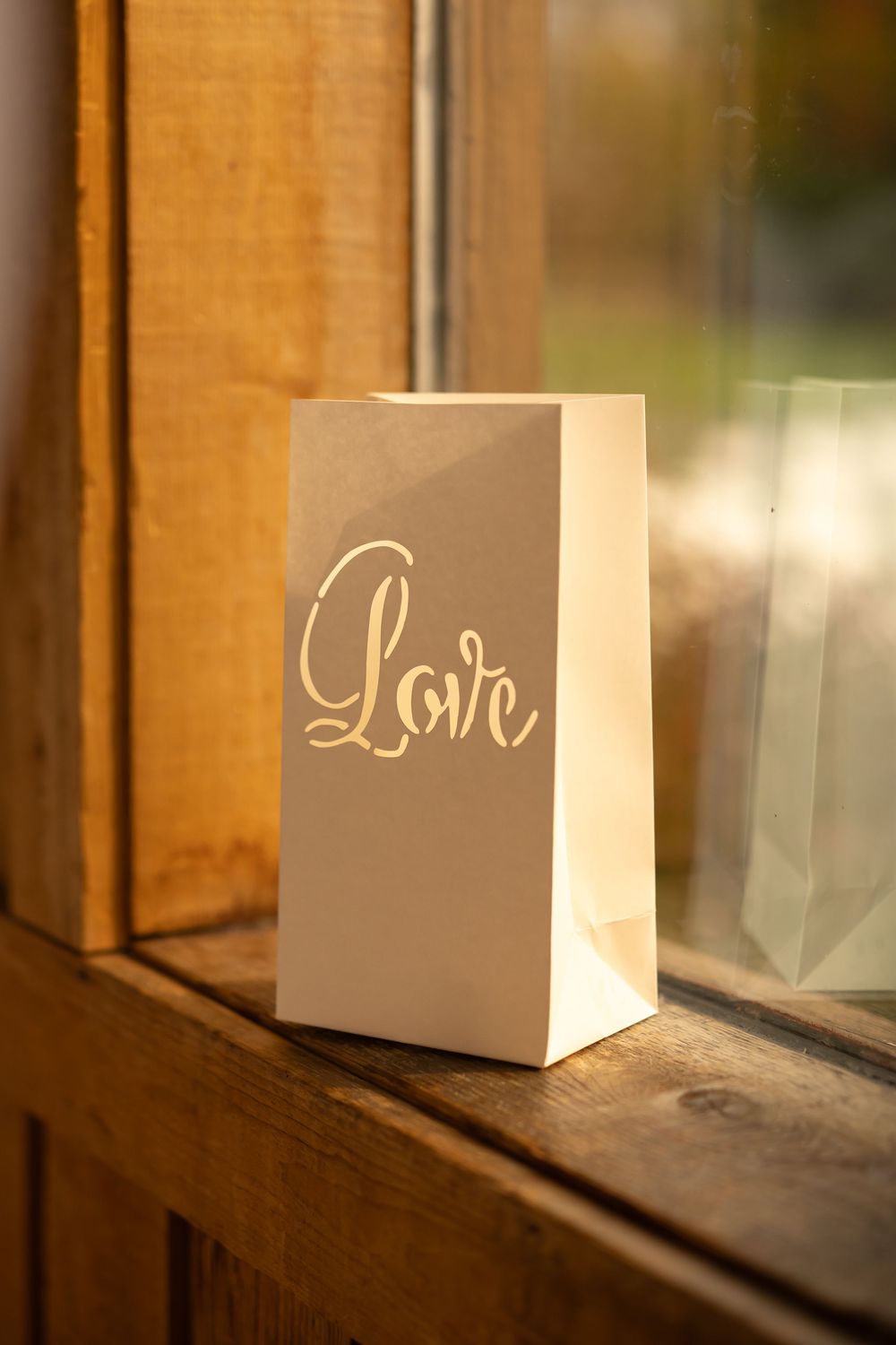 A decorative white box with 'Love' text sits on a rustic wooden windowsill in warm sunlight.
