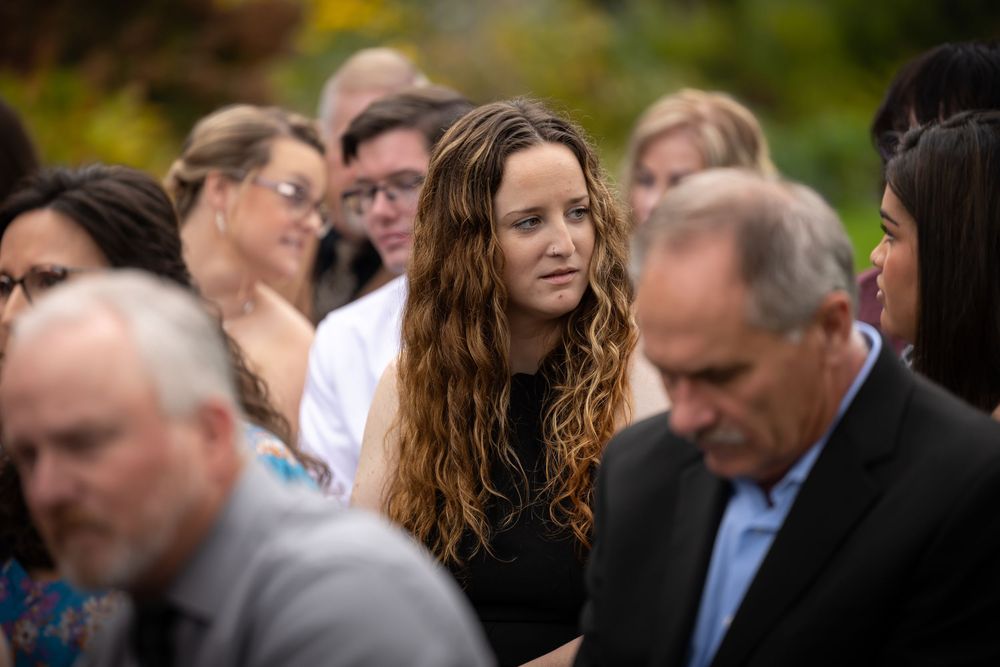 Wedding guests gather outdoors with one attendee with wavy hair standing out in the crowd.