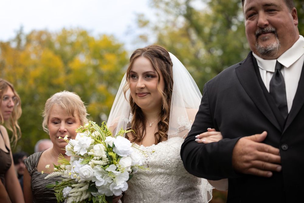 Wedding ceremony celebration with guests and couple under wooden arbor with fall foliage.