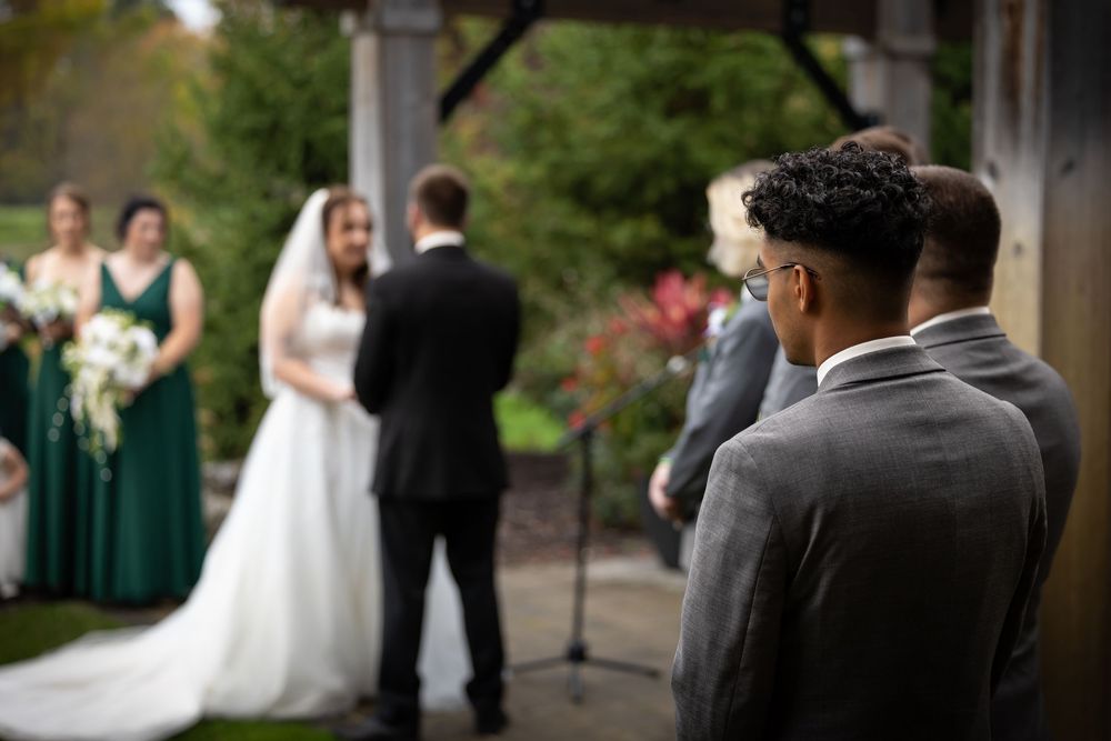 Wedding party poses together outdoors with bridesmaids in emerald green dresses and groomsmen in black suits.