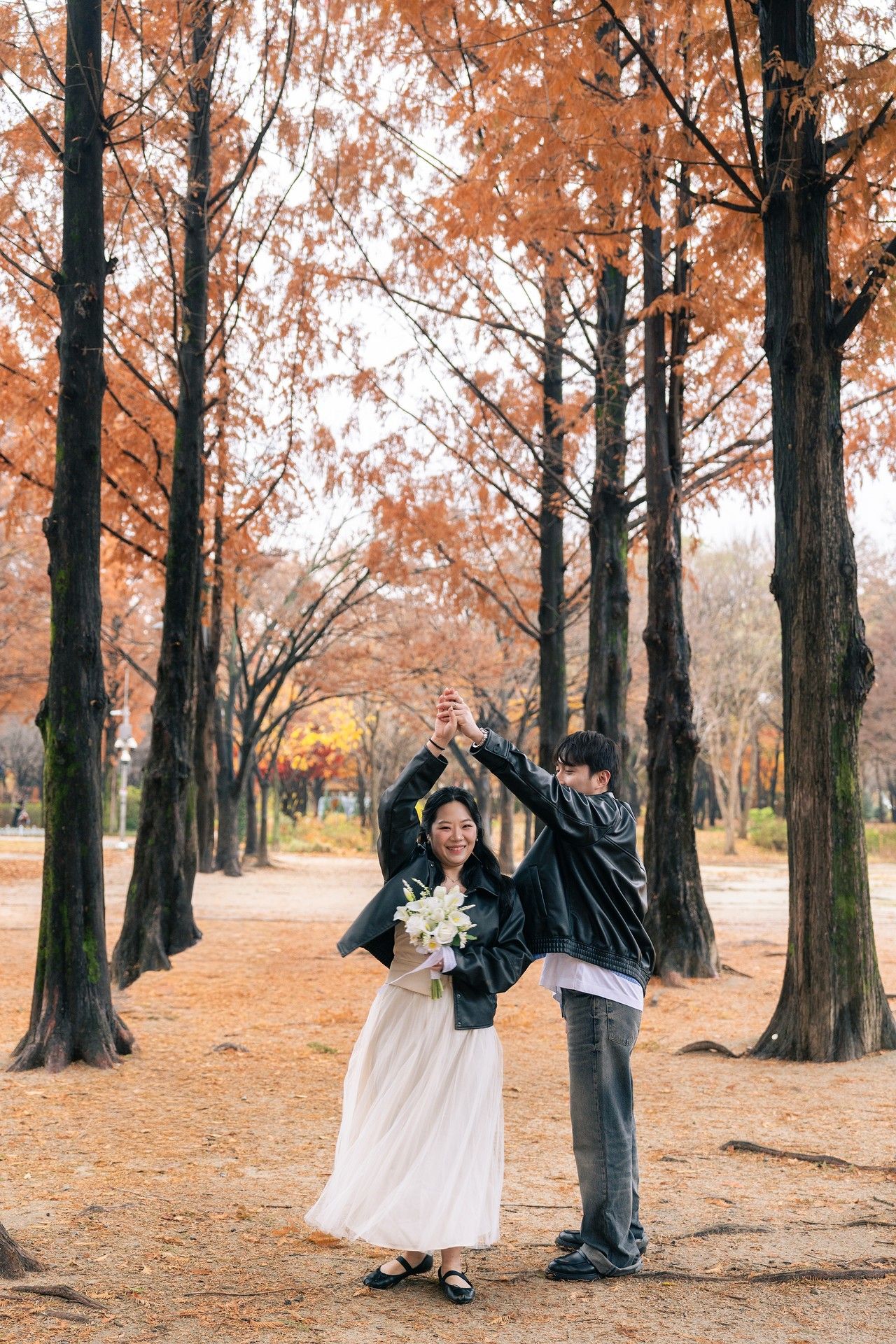 Couple dances playfully among autumn trees with orange leaves in a romantic outdoor photoshoot.