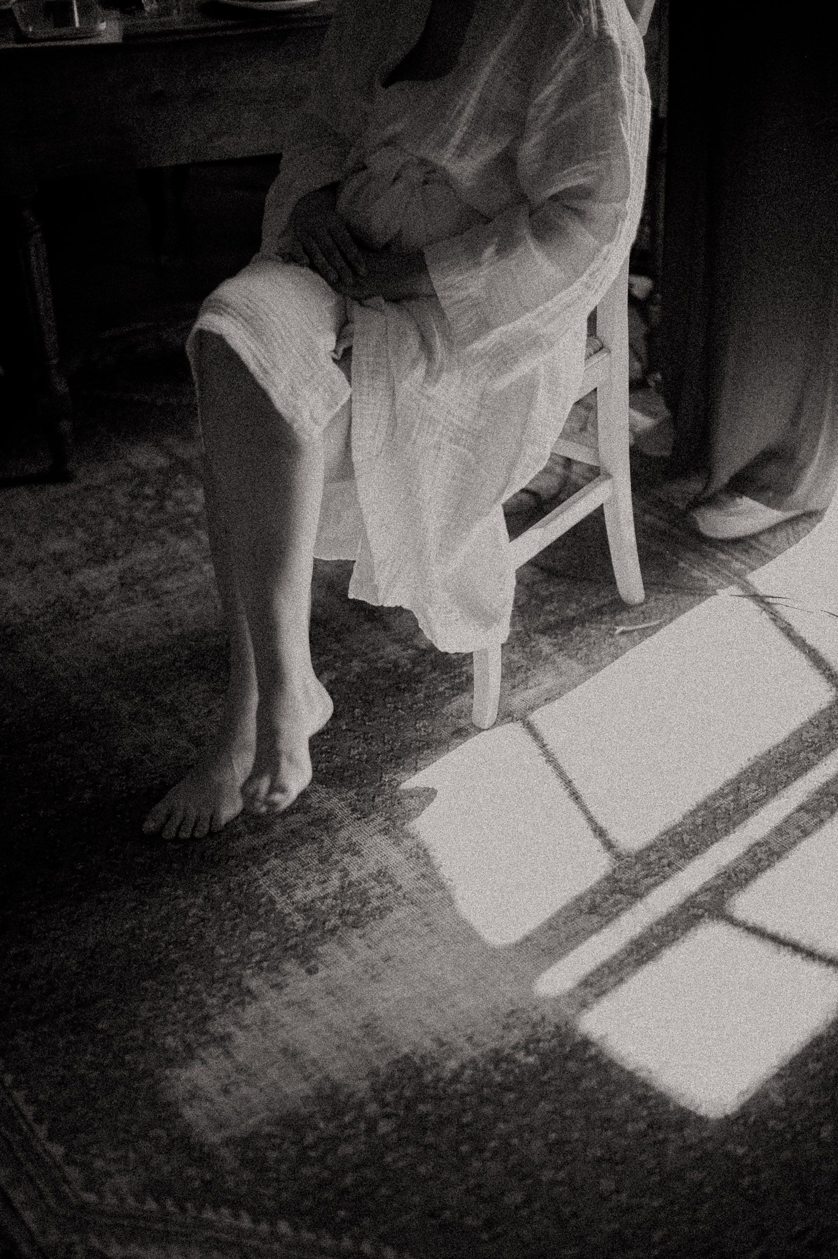 Black and white image of bare feet casting shadows on a textured carpet through window light.