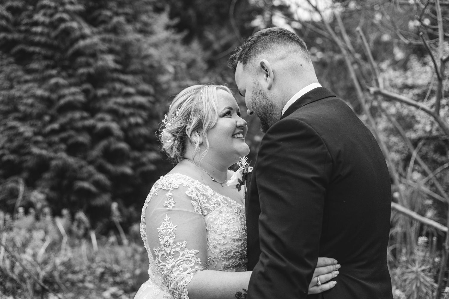 A tender black and white wedding moment captured between a couple sharing an intimate embrace in a garden setting.