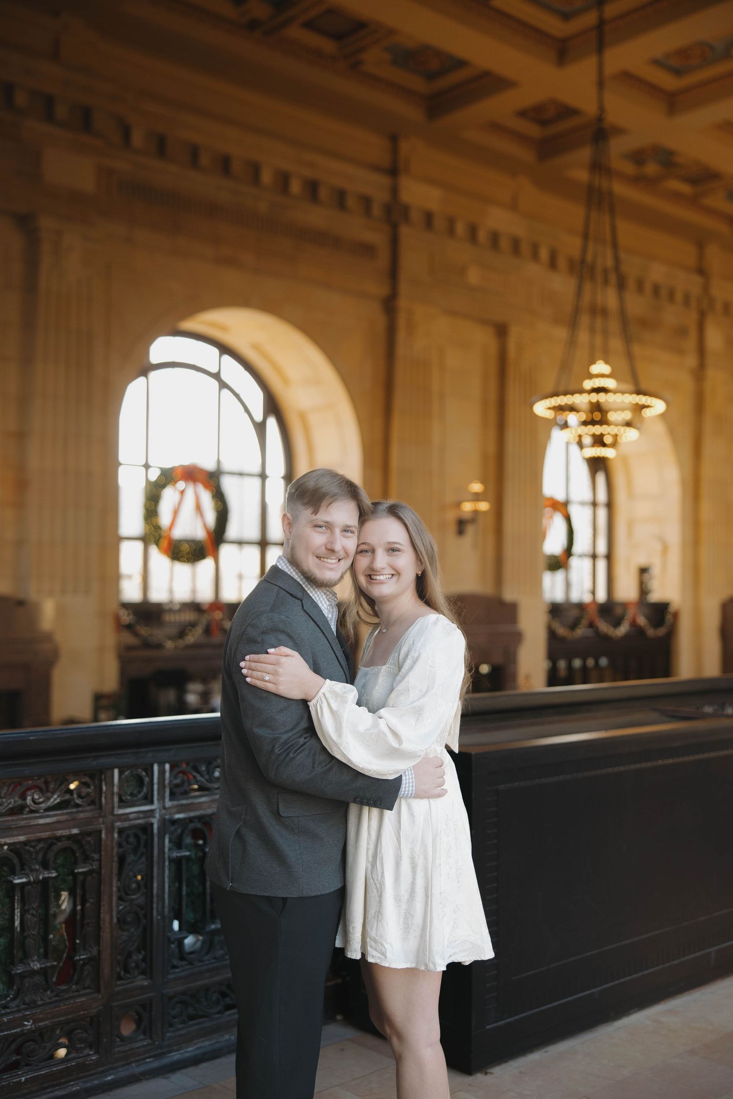A couple shares a romantic moment in an elegant historic building with ornate architecture and grand lighting.