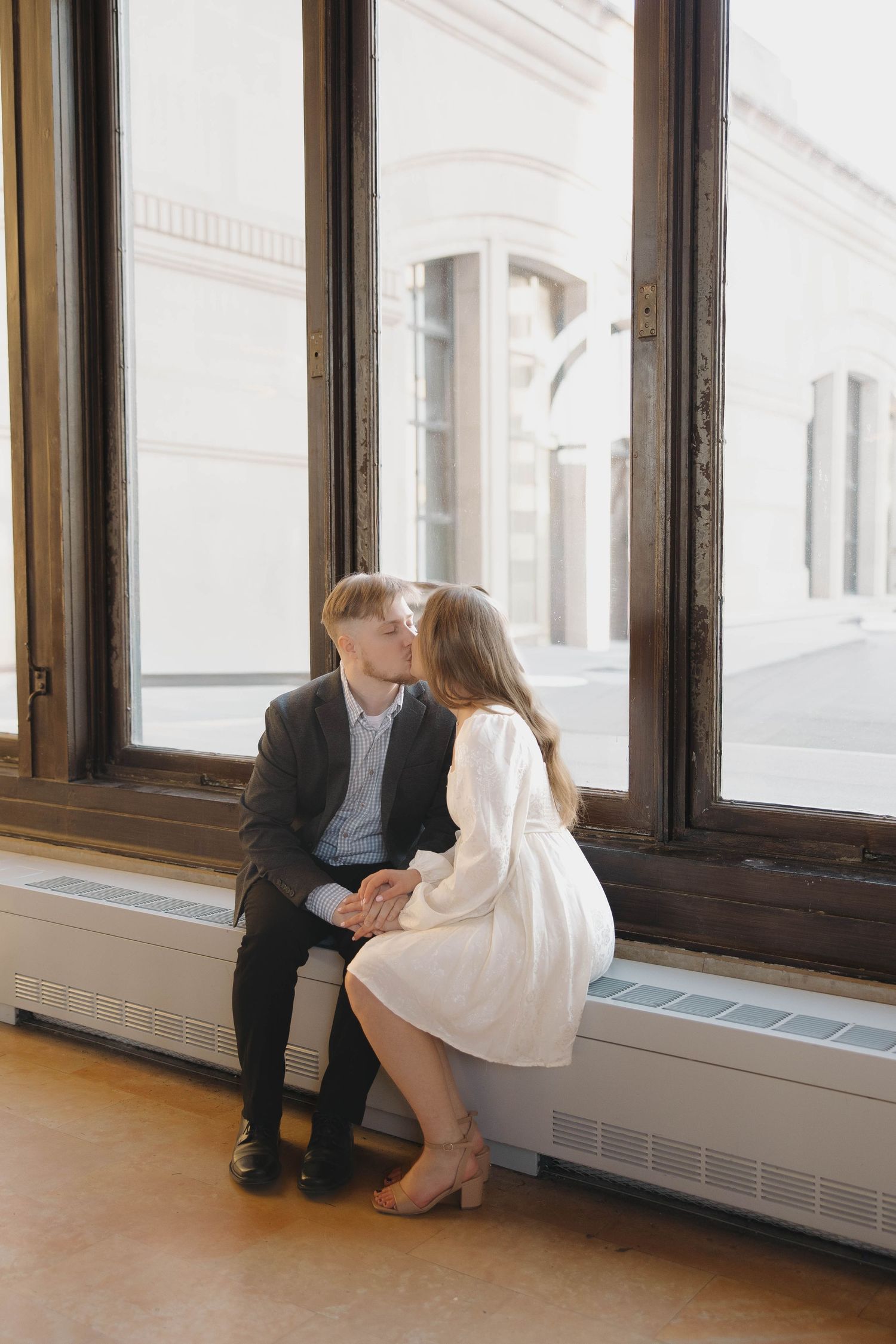 Two people sit together on a windowsill in a bright white room with dark wood trim.