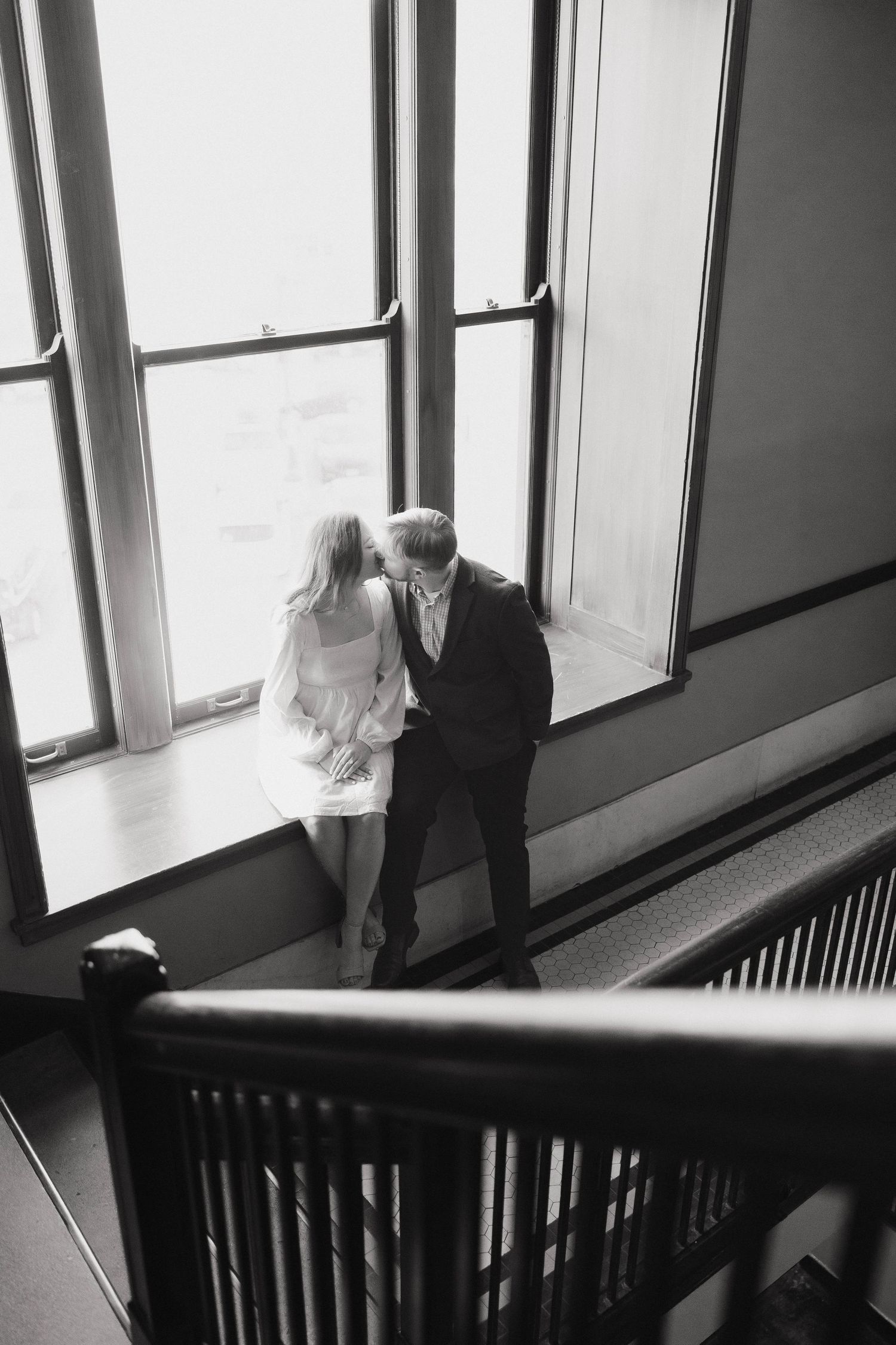 A black and white photo series showing intimate moments near large windows in a historic building.