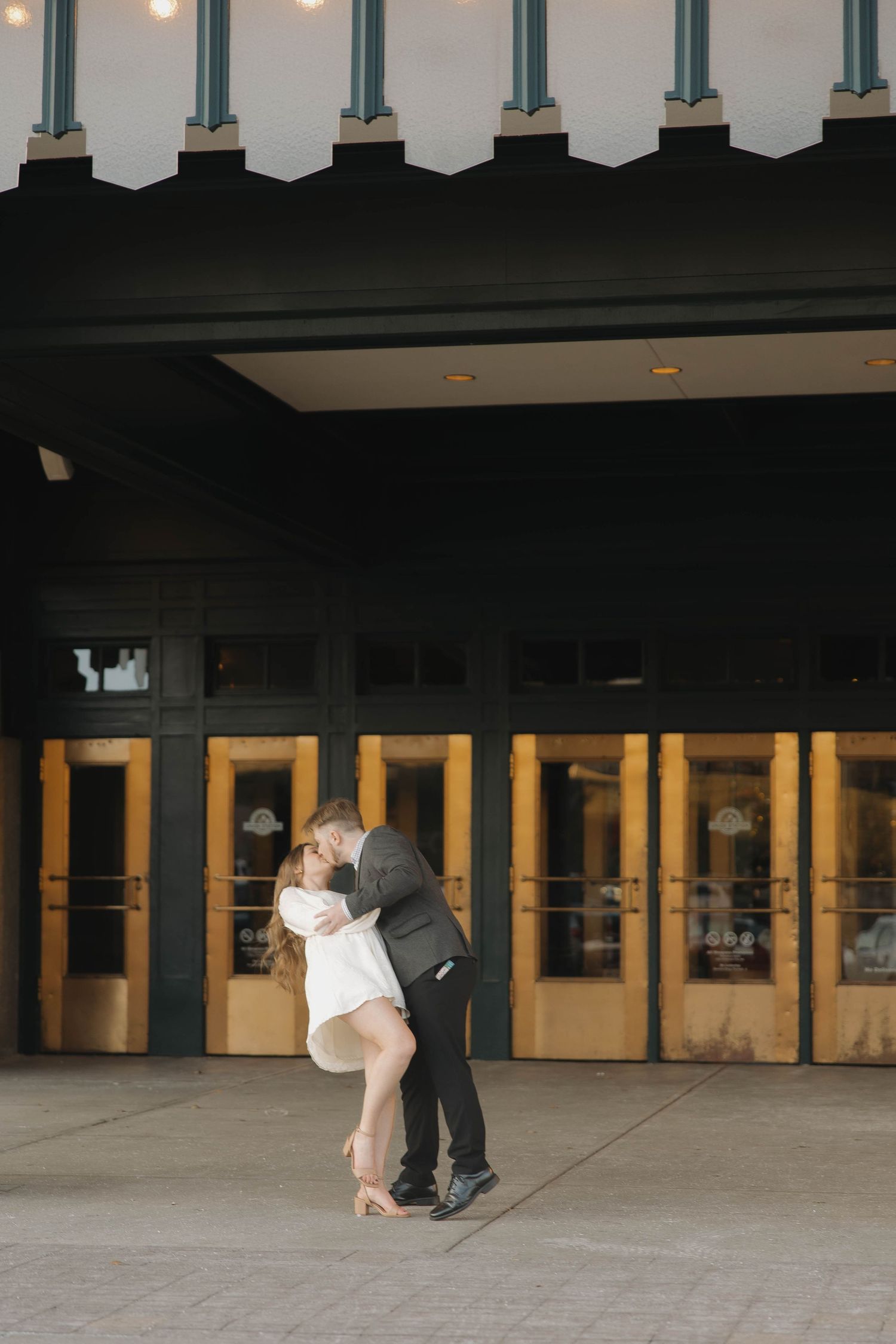 A couple dances in an elegant ballroom, with the woman in white being gracefully dipped by her partner.