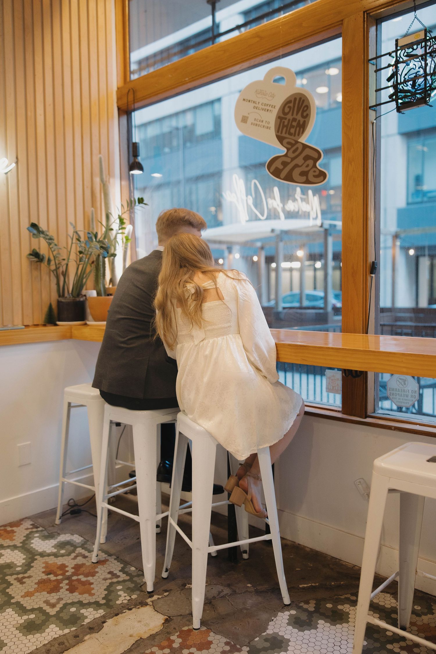 People seated at a window counter bar with white stools in a modern cafe interior.