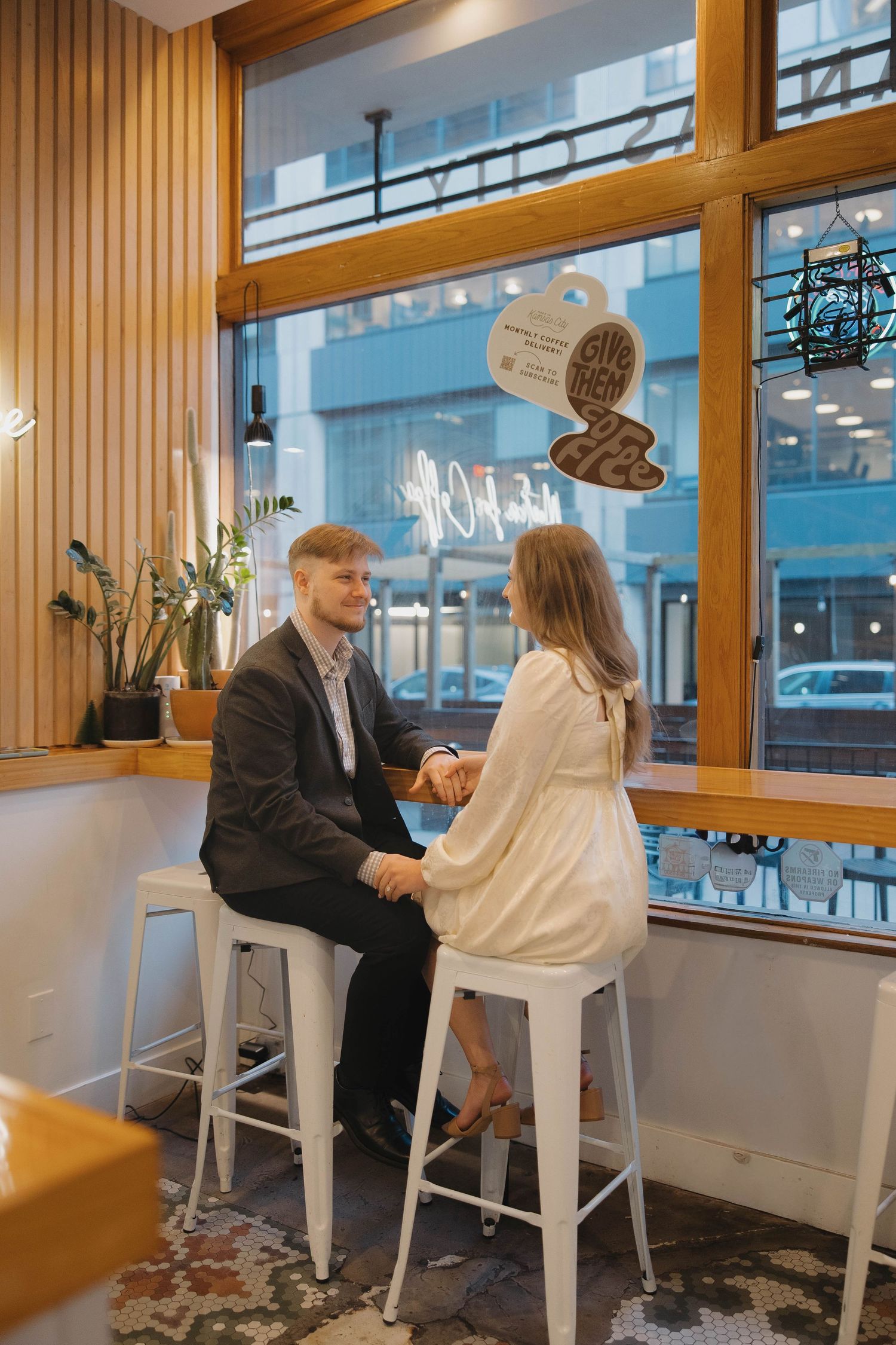 Two people sit at a bar counter with wooden paneling and white stools, engaged in conversation in a modern setting.