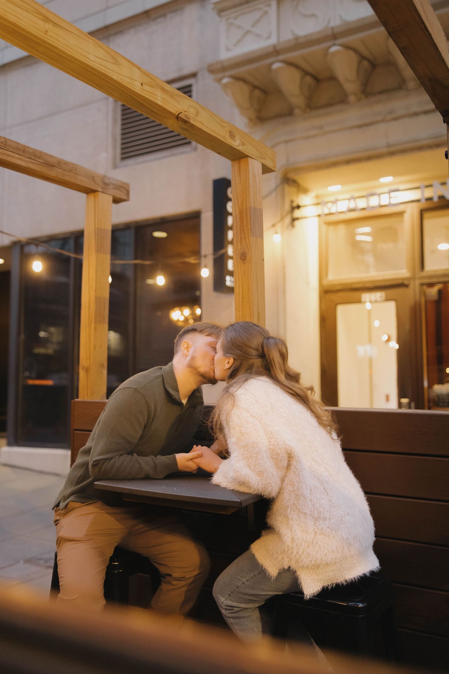 A romantic moment shared on a bench in a warmly lit indoor space with wooden beams and pillars.