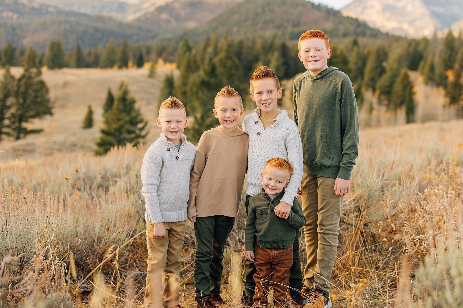 Group portrait in casual earth-toned clothing against mountain backdrop with evergreen trees.
