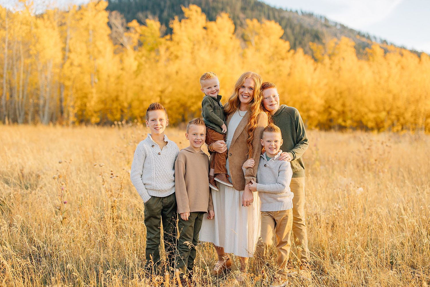 A group stands together in a golden autumn field at sunset with tall grass and mountains in the background.
